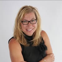 428693249_10229409765735931_3598352112306605808_n | Paragon Wealth Management Smiling blonde woman with glasses in a black sleeveless top, standing against a light background.